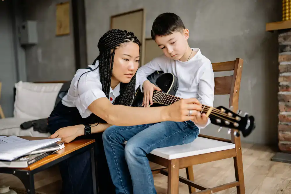 A student smiling while playing an acoustic guitar during a lesson